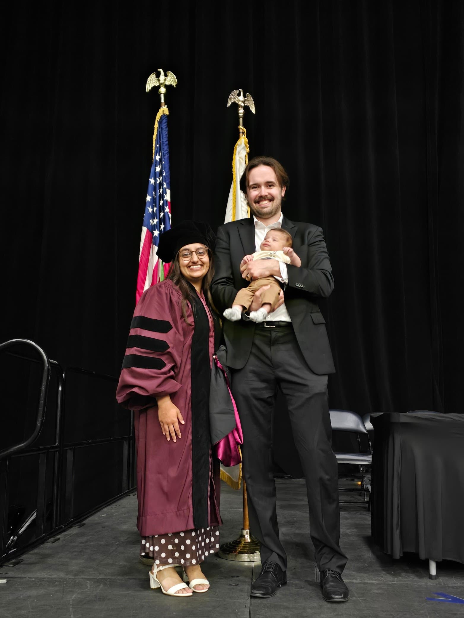 Braden Bisping holding his son James, standing beside his wife Jessica in her doctoral graduation gown